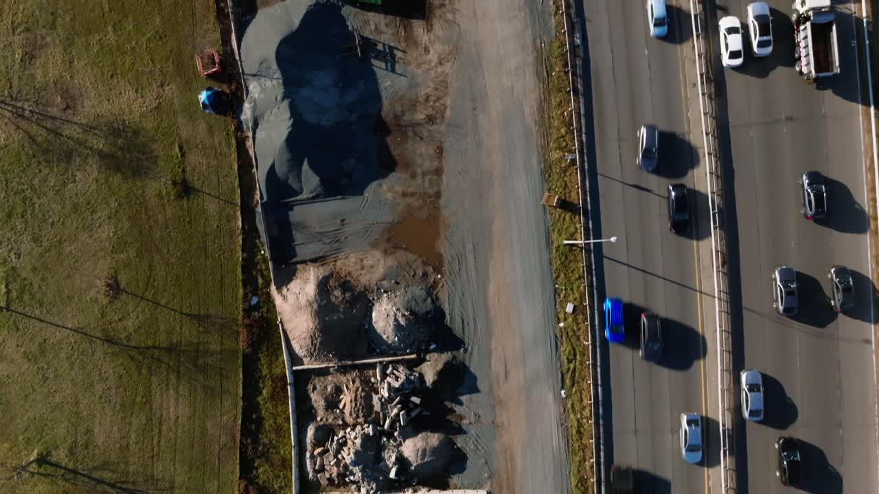 una vista de arriba hacia abajo sobre un sitio de construcción con equipos y vehículos entre el belt parkway y un parque en brooklyn, ny en un día soleado