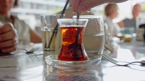 la persona toma una cuchara y la gira en una taza de té mientras está sentada en el restaurante, vista de cerca