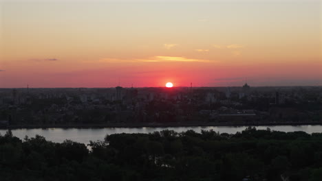 stunning sunset over a city skyline with a river reflecting the warm evening light, aerial tracking with orange pink hues