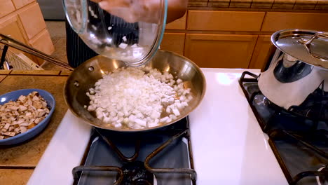mujer agrega cebollas picadas, champiñones y pimienta a la sartén en la cocina, primer plano