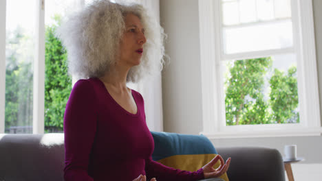 Senior-caucasian-woman-practicing-yoga-while-sitting-on-the-couch-at-home