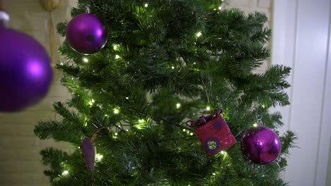 hombre adulto joven colgando decoración púrpura en el árbol de navidad durante la temporada de vacaciones