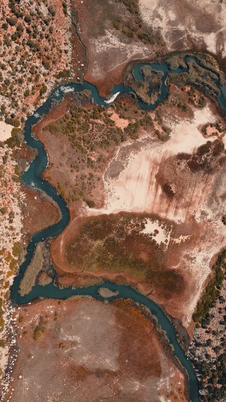 Aerial drone social media style top down video showing meandering river cutting through sandy flats and vegetated patches near Dalyan Delta in Mugla Province during bright warm daylight