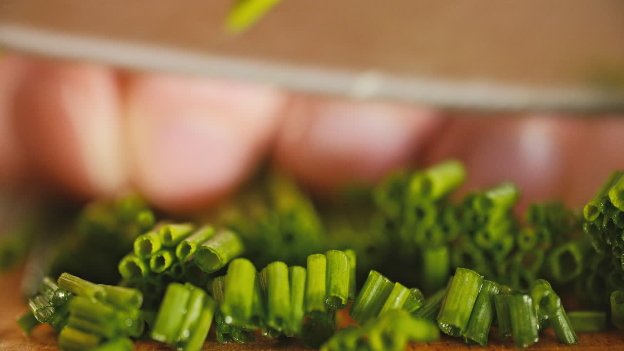 foto macro de un montón de cebolletas frescas sobre una tabla de cortar de madera, luego una mano masculina comienza a cortarlas