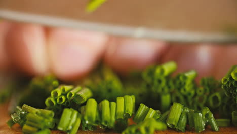 foto macro de un montón de cebolletas frescas sobre una tabla de cortar de madera, luego una mano masculina comienza a cortarlas