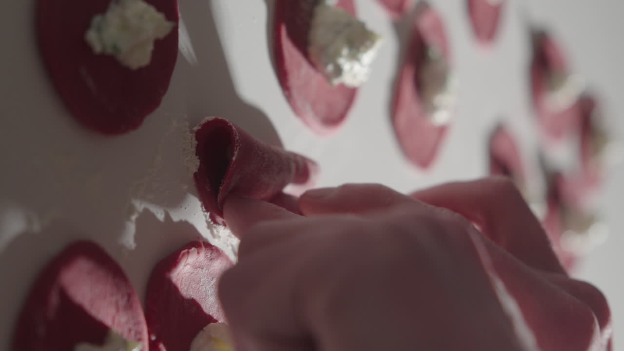 Formazione a mano di tortellini freschi fatti in casa con barbabietola. Primo piano verticale 4K.