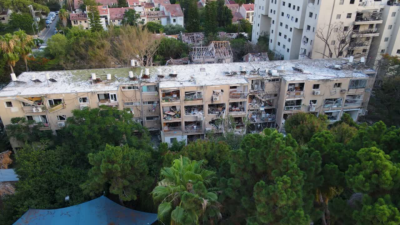 High drone shot advancing toward shattered buildings in Tel Aviv, showing destroyed interiors, debris and dust-covered facades.