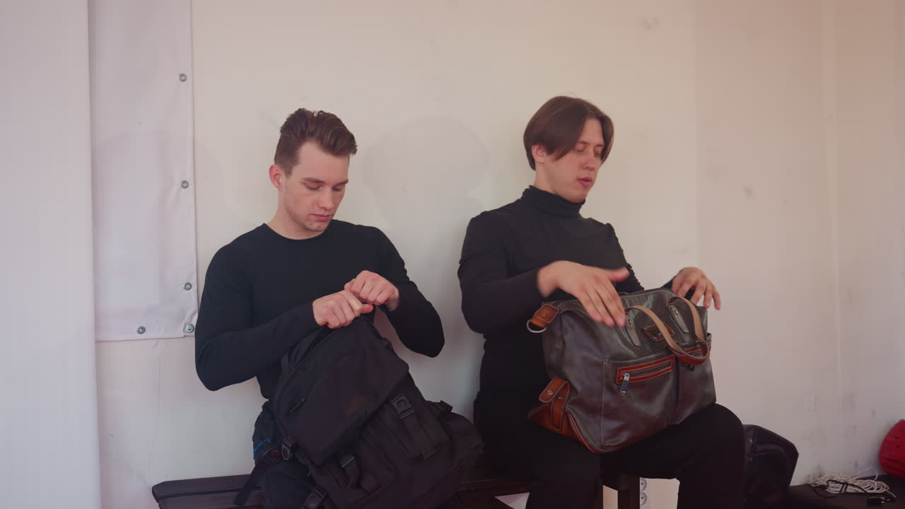 Policemen in black uniforms sitting on bench inside gym unpacking sports bags, preparing training gear, holding boxing gloves, getting ready for workout session with determination