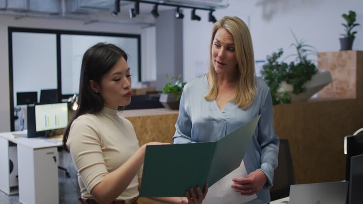 Caucasian and Asian women review business documents in an office
