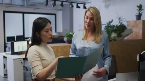 caucasian and asian women review business documents in an office