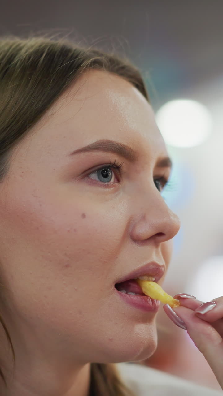 Close-up of lady eating fries with a focused look, soft bokeh background with colorful blinking lights in a lively shopping mall setting