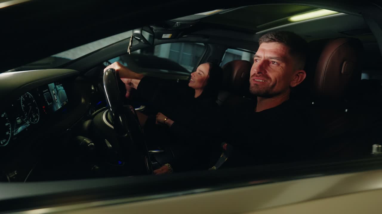Happy couple sharing a moment inside luxury car during nighttime drive, captured through driver’s side window.