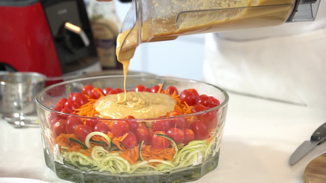 Pouring almond butter orange juice sauce onto zucchini noodles zoodles adding to bowl healthy vegan vegetarian lifestyle diet detox