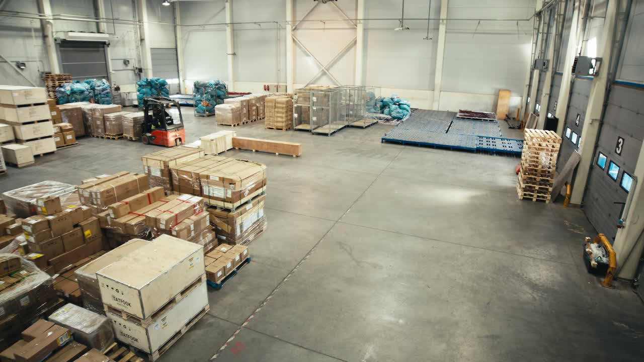 Red forklift driving around modern well arranged warehouse with shipment load. Panning high angle shot.