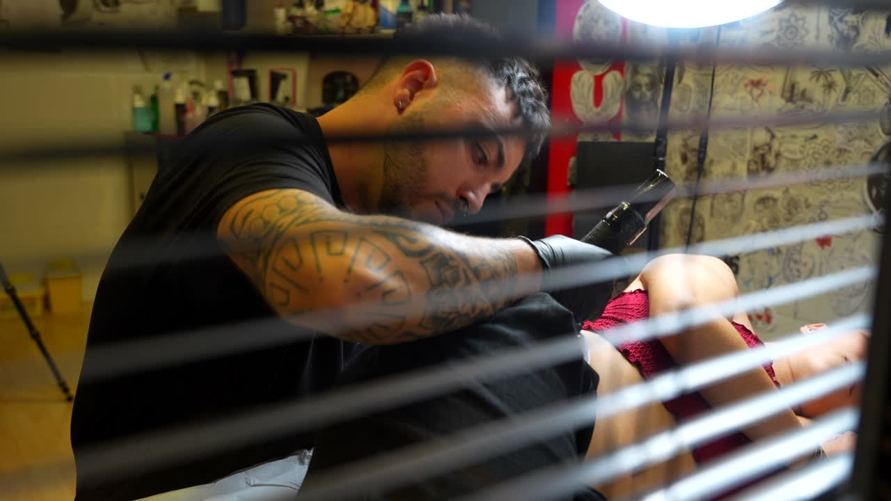Tattoo artist working on a design through a window in a studio. Close-up angle