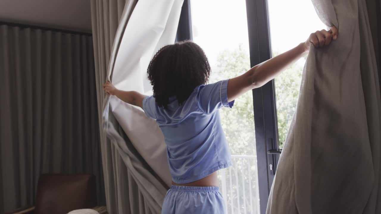 Una persona tocca le tende alla finestra, spostandole per far entrare la luce del giorno e guardare fuori.