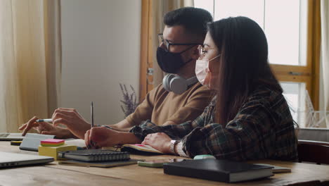 Vista-Lateral-De-Un-Estudiante-Con-Auriculares-Hablando-Con-Una-Compañera-En-La-Mesa-Discutiendo-Sobre-Un-Proyecto-Usando-Una-Laptop