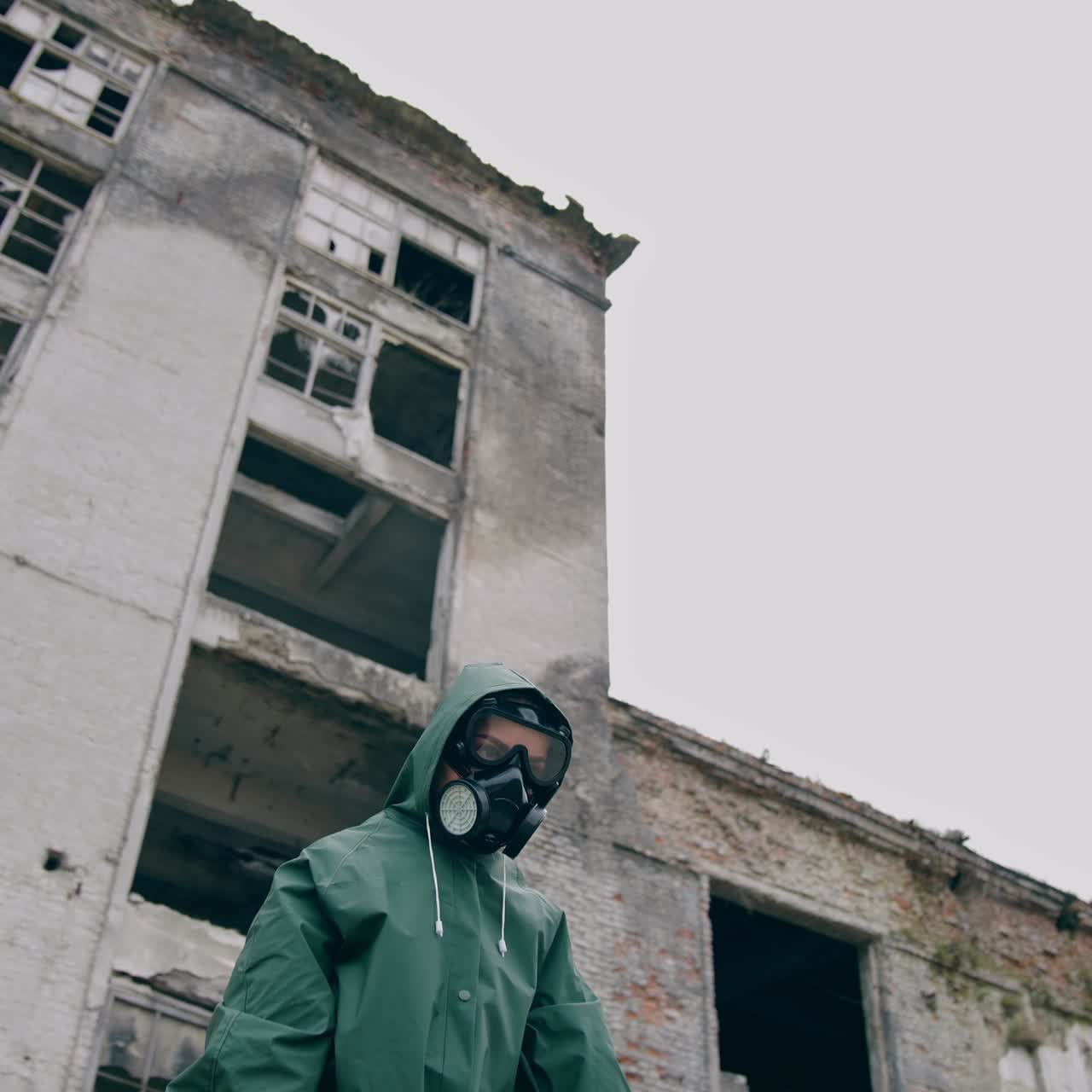 Abandoned place and a person in safety suit. Survivor in gas mask and hazmat suit standing with stretched arms on ruined building background. Chemical catastrophe