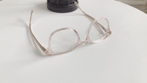 Modern-eyeglasses-in-light-colour-lie-on-a-white-table,-bright-glasses-frame,-slow-motion-footage