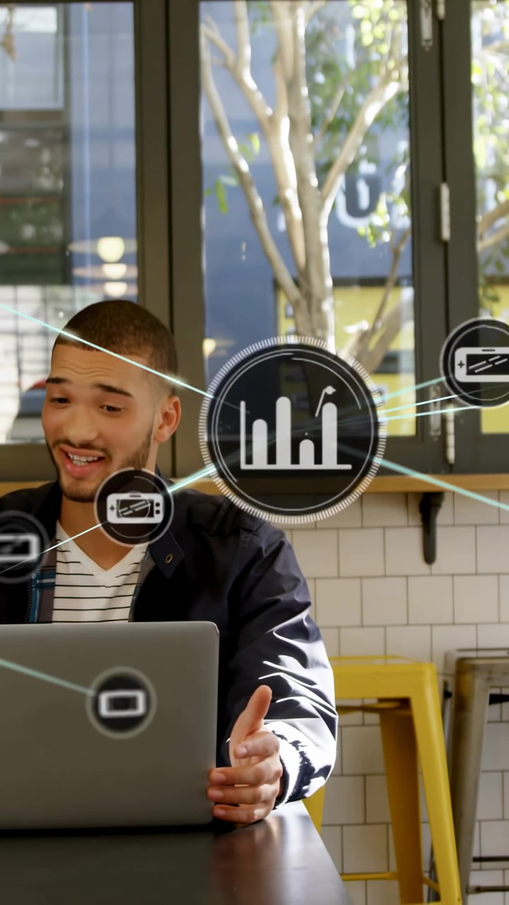 Vertical video: Man typing and gesturing on laptop in cafe, HUD icons forming to show business data