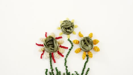 Colored-flowers-shape-formed-by-various-pasta-on-white-background