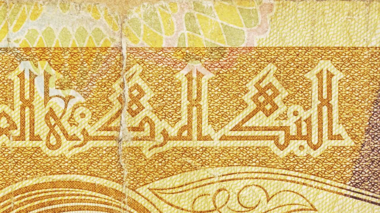 Macro pan along an Iraqi banknote showing Arabic calligraphy for the Central Bank with gold guilloche and aged paper texture