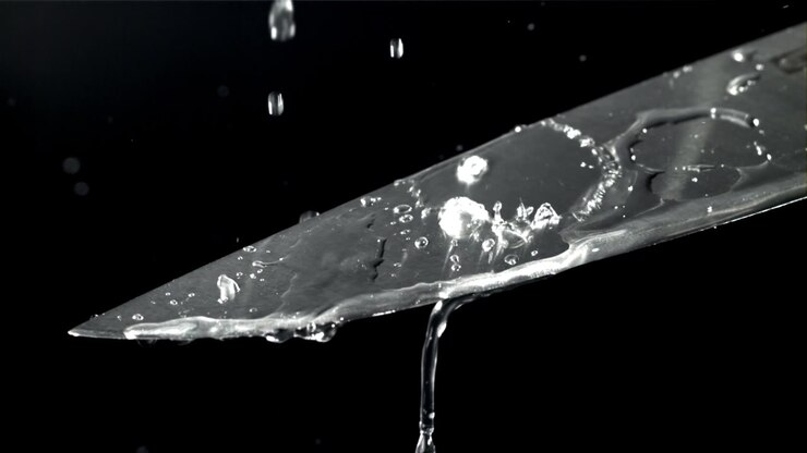 Acqua che schizza e gocciola su una lama di coltello al rallentatore
