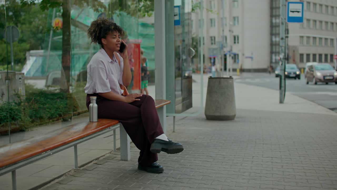 Donna che parla al telefono a una fermata dell'autobus in città