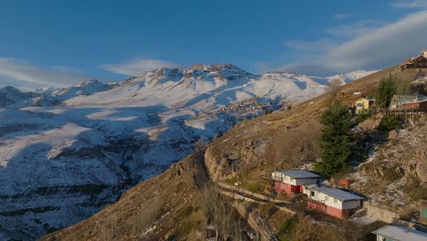 Aerial-establishing-shot-of-the-Farellones-in-the-distance-on-a-snowy-Andean-Mountain