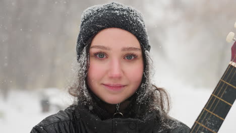 young lady standing in serene winter setting wearing black jacket and beanie, snowflakes softly resting on her hair, blurred figure walking in background