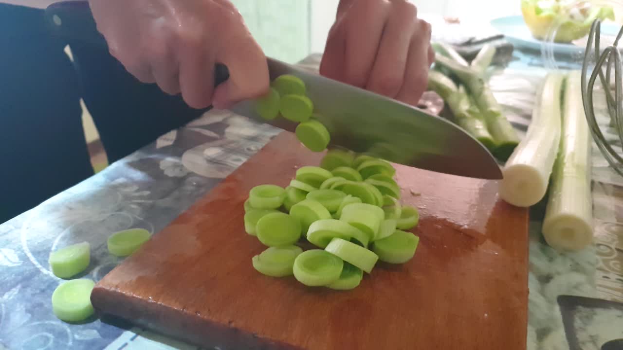Closeup footage of home kitchen table with woman slicing onions on the wooden cutting board