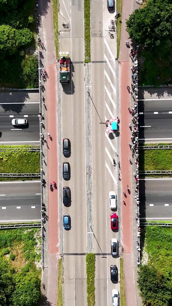 Aerial view of a cycling event on a multi-lane road with spectators lining a bridge