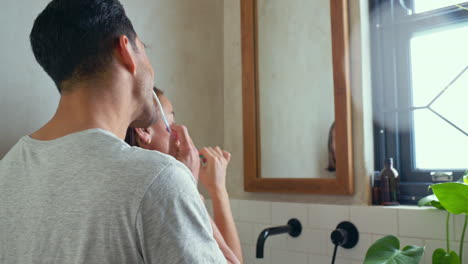 couple brushing teeth in home bathroom mirror