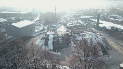 aerial shot of sawmill with wood logs and tree cranes working in winter season