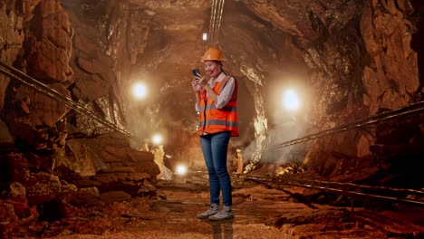 full body side view of asian female engineer with safety helmet using smartphone in underground mine tunnel