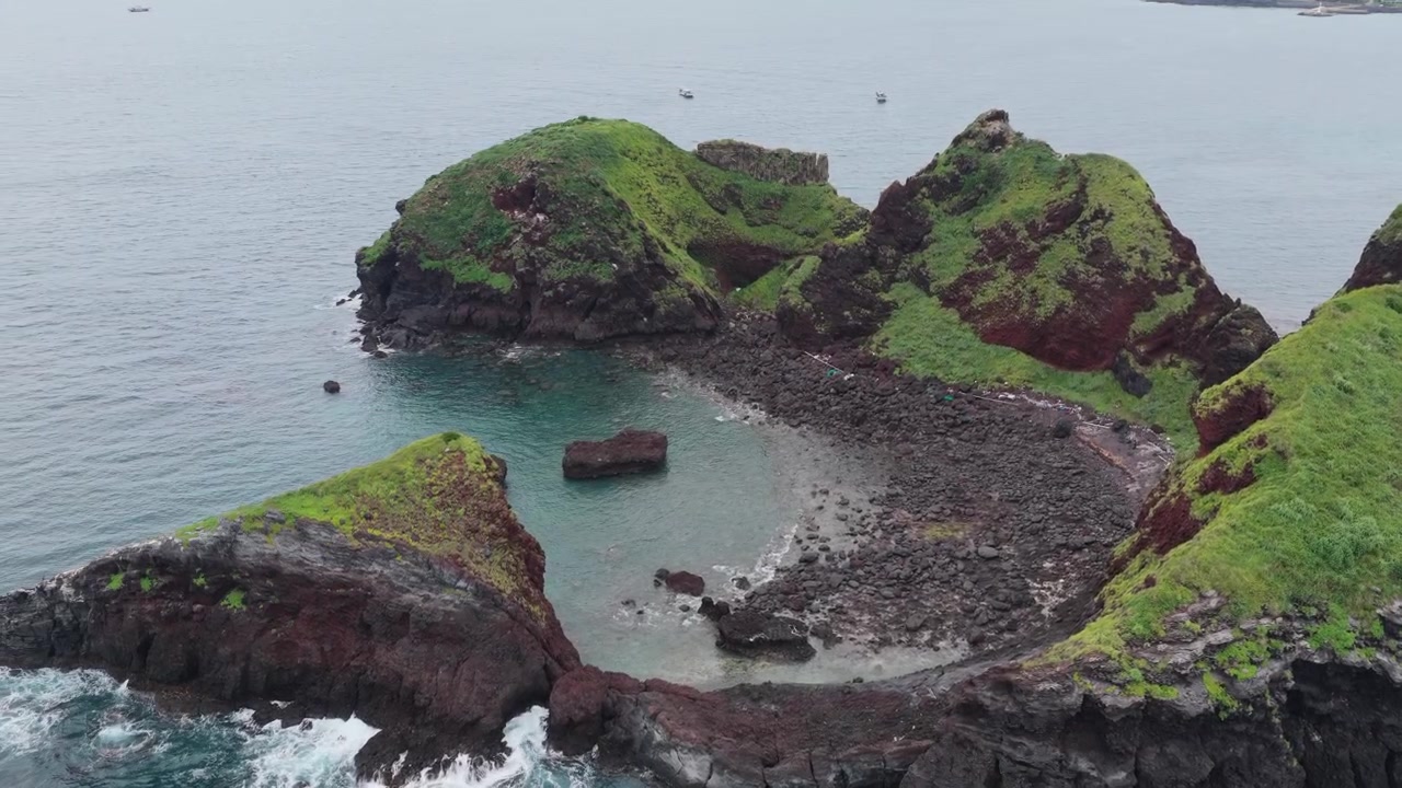 Vista aérea horizontal de los islotes de Chagwido cerca del Sendero Costero Eongal en la Isla de Jeju, Corea del Sur, con la cámara paneando a la izquierda sobre formaciones rocosas volcánicas y una cala protegida