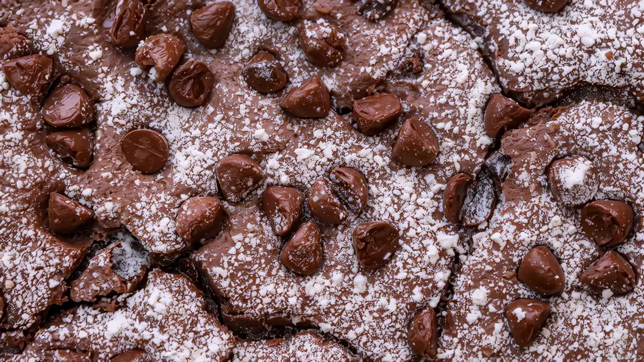 Panoramische camera die een brownie van bovenaf laat zien, verschuivende halfzoete chocoladechips, met nadruk op poedersuiker