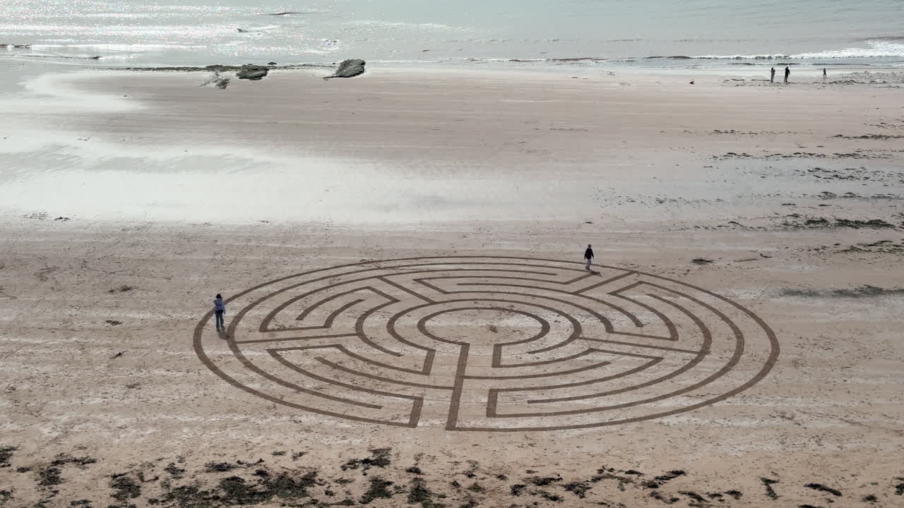 A large Labyrinth drawn on the beach at Sandy Bay, Devon, England with visitors exploring the art work