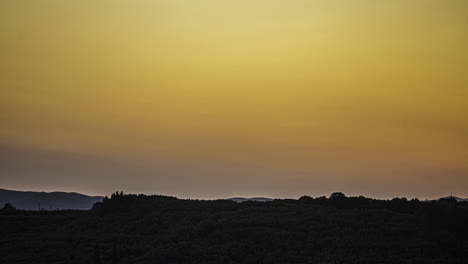 Soft-orange-red-yellow-glow-of-light-recedes-across-sky-above-grassy-hill