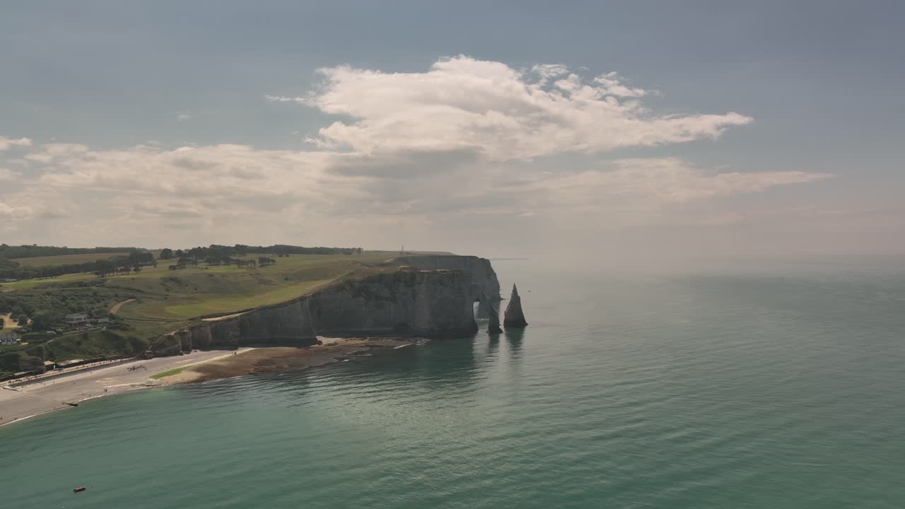 Aerial drone shot of Étretat cliffs and beach in France with a majestic sailing ship moving through the ocean, highlighting dramatic coastal scenery and natural beauty