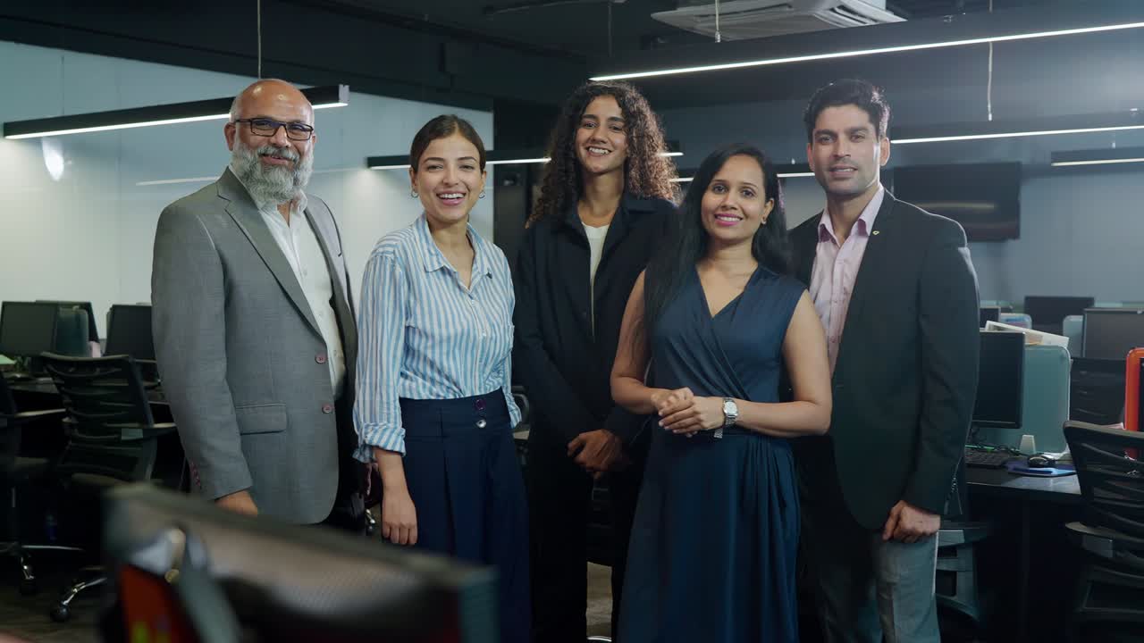 un grupo de indios de género mixto en una oficina corporativa sonriendo.
