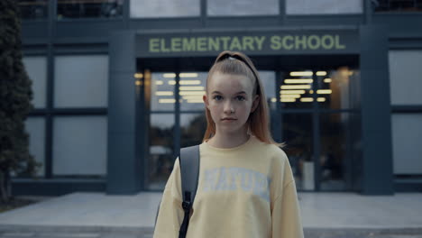 Portrait-elementary-age-girl-posing-at-school-entrance.-Student-looking-camera.