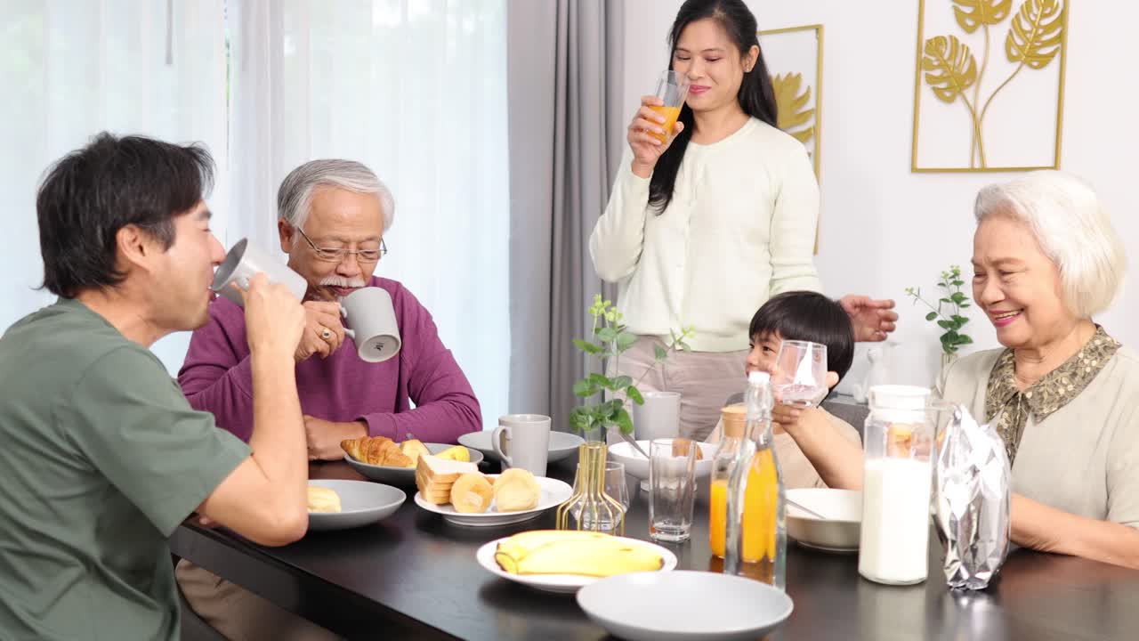 Four generations share breakfast, smiling and toasting drinks in bright, cozy dining room setting