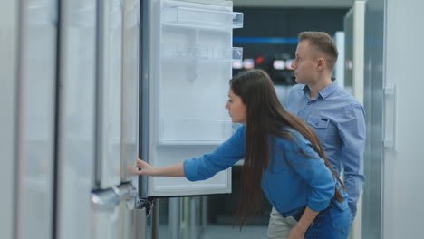 a man and a woman open the refrigerator door inspect the design and quality before buying in the store