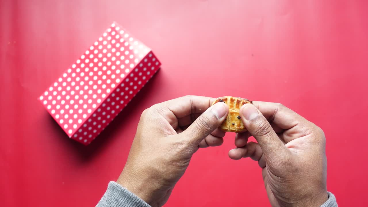 persona sosteniendo una galleta sobre un fondo rojo con una caja de puntos de polca blanca