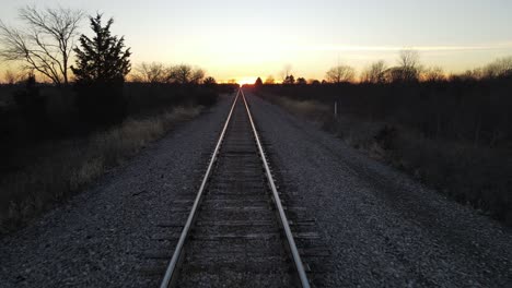 las vías del ferrocarril de acero brillan debido al resplandor del atardecer, dolly vista hacia atrás