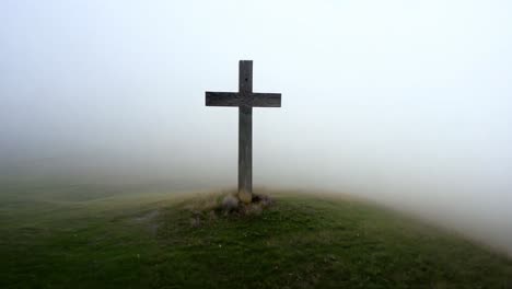 fog envelops a wooden cross atop a hill, surrounded by lush green grass, creating a serene and spiritual atmosphere