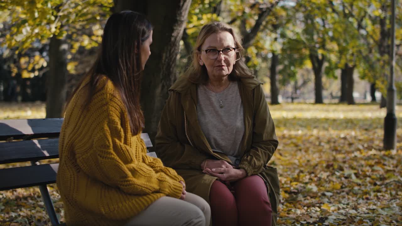 Kaukasiske kvinder sidder sammen på en bænk i parken om efteråret