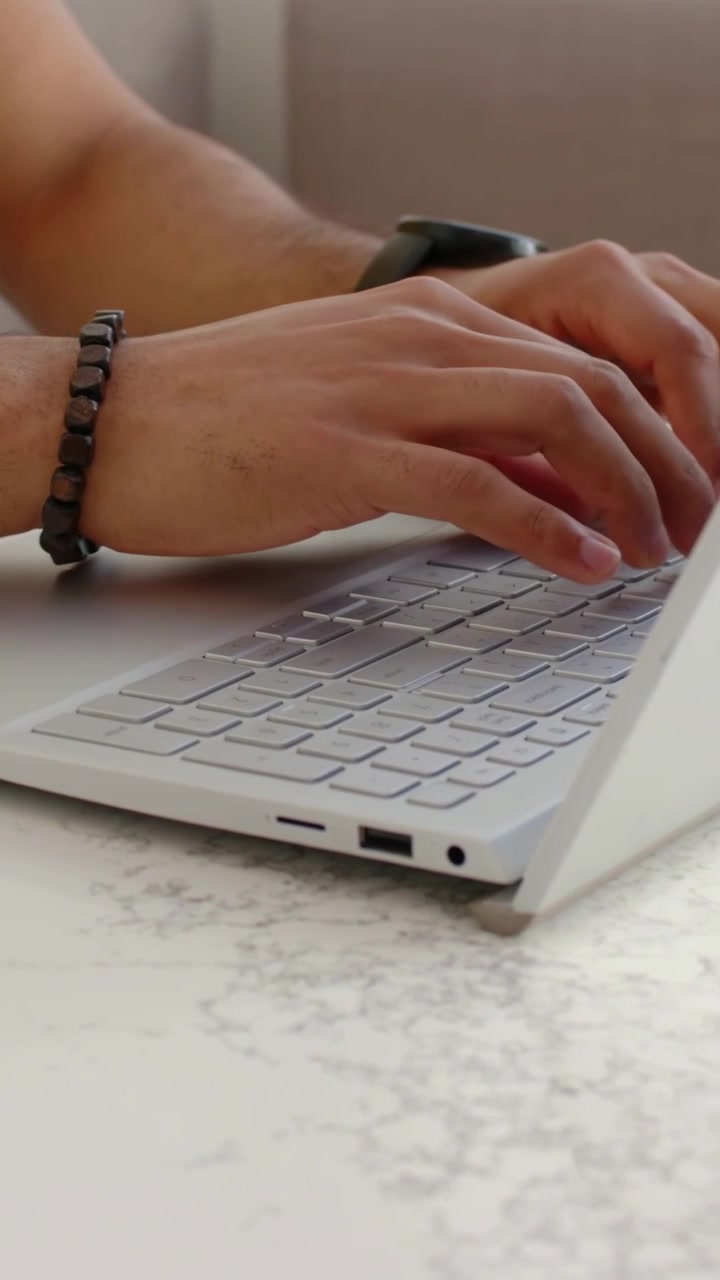 Vertical video: Shifting, man in yellow tee typing on laptop at counter for work, beige mug near