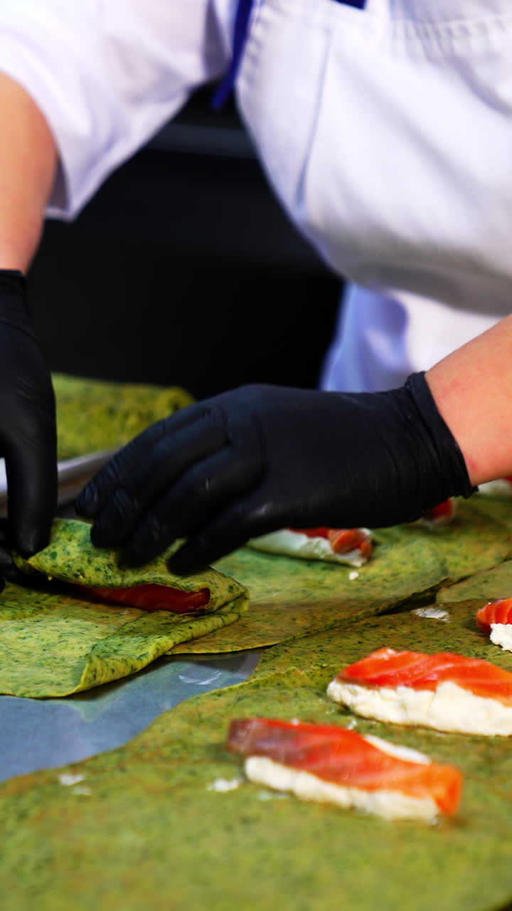 Unusual green crepes are rolled with cheese and salmon fish. The cook rolls the pancakes and lays them on the tray. Close up. Vertical video